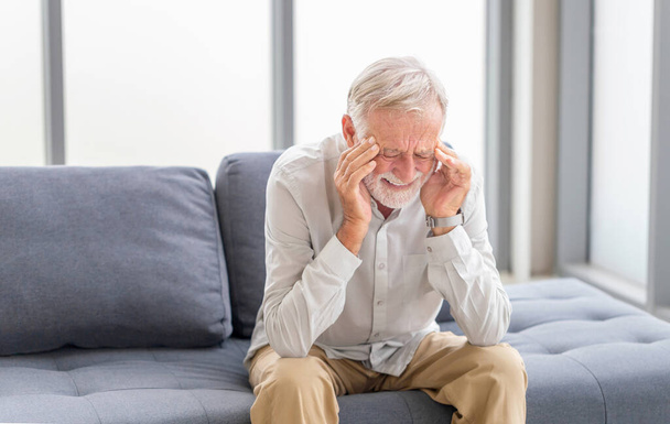 Idős férfi, akinek fejfájás és megérinti a fejét, miközben szenved a migrén a nappaliban, érett férfi nyomja a kezét a fejét szenved elviselhetetlen fájdalom - Fotó, kép