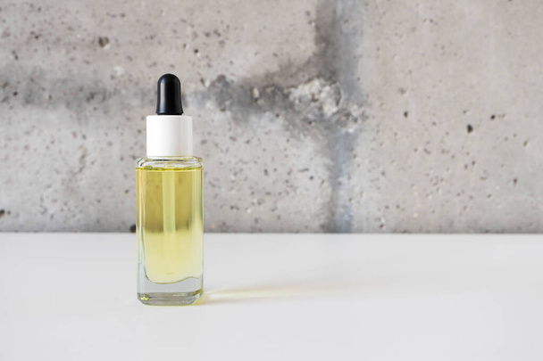 Botella de cristal de suero facial natural con pipeta sobre escritorio blanco sobre fondo de pared de cemento - Foto, Imagen