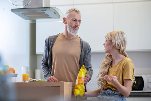 A blonde girl sitting in the kitchen and talking to her dad - Photo, Image