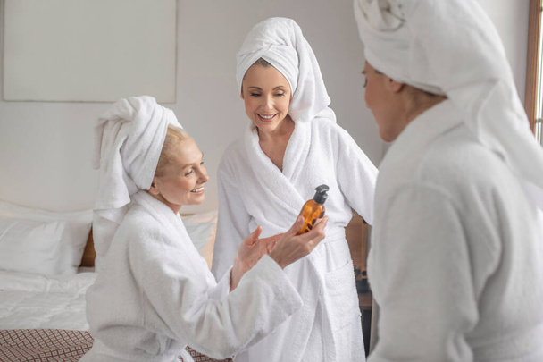 Women in bathrobes discussing new cosmetic product - Foto, Imagen