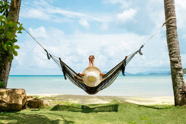 Koncepcja wakacji letnich. Szczęśliwa kobieta w czarnym bikini relaksująca się w hamaku na tropikalnej plaży - Zdjęcie, obraz