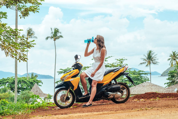 Portrait of young woman on scooter drinking water from reusable bottle - Foto, afbeelding