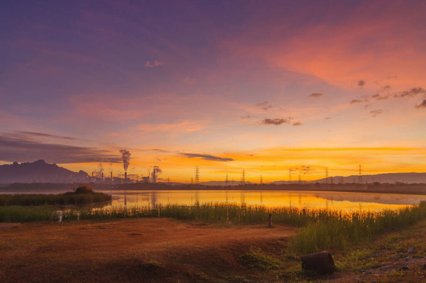 Centrale elettrica a carbone e riflessione dell'acqua nella splendida mattinata tra montagne e laghi. Mae Moh, Lampang, Thailandia. Linee una fila polo ad alta tensione. - Foto, immagini