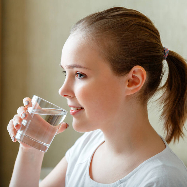 Smile young woman drinks glass of pure water in morning after waking up. Happy teen girl maintains water balance for body health by drinking transparent cup of clean water. Square Close up - Photo, image