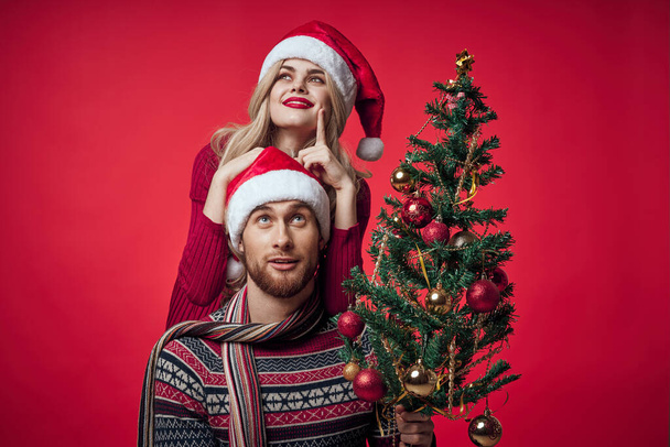 junges Ehepaar Weihnachtsbaum Spielzeug Urlaub Freude roter Hintergrund - Foto, Bild