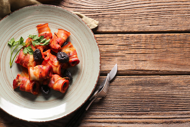 Talíř s chutnými švestkami pečené v křupavé slanině na dřevěném pozadí - Fotografie, Obrázek