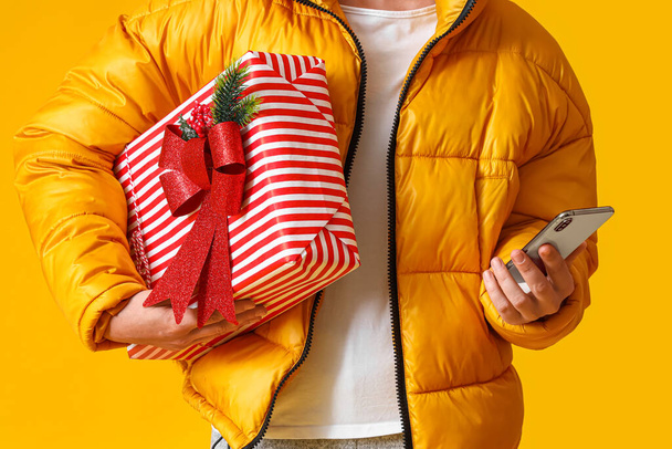 Muž s vánoční dárkové krabice a mobilní telefon na žlutém pozadí - Fotografie, Obrázek