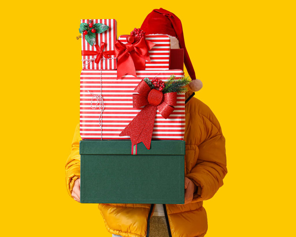Man in Santa hat holding Christmas gift boxes on yellow background - Photo, Image