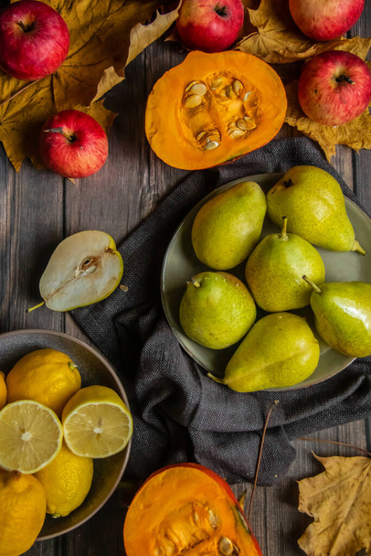 podzimní zátiší hrušek, jablek, dýní, citronů a žlutých listů na dřevěném stole - Fotografie, Obrázek
