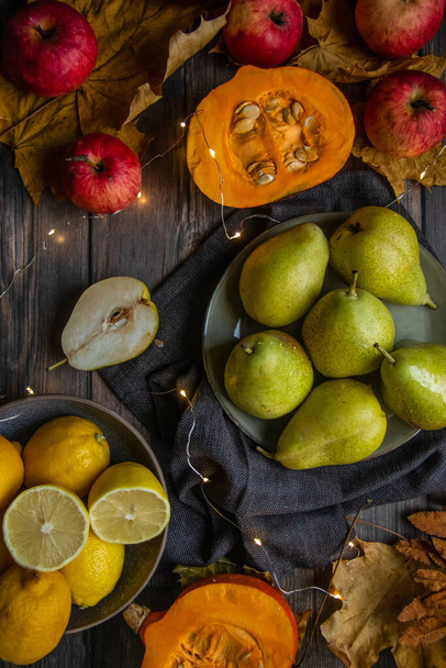 autumn still life of pears, apples, pumpkins, lemons and yellow leaves on a wooden table - Фото, зображення