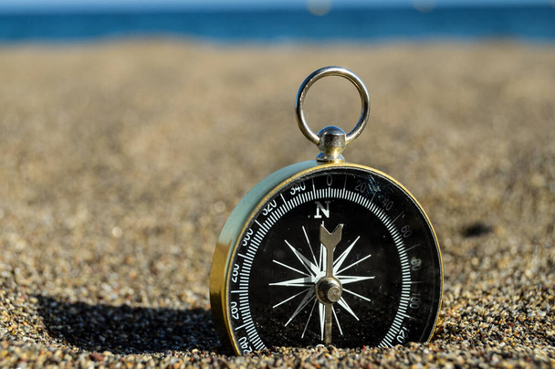 A closeup shot of a compass half-buried in the sand near a sea in Spain - Fotó, kép