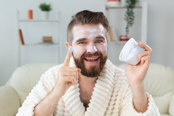 Bearded guy applying facial cream in front of mirror Skin care and spa for man concept. - Fotografie, Obrázek