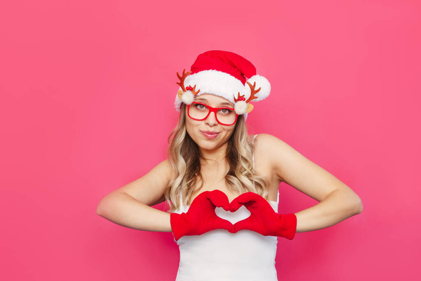 beautiful young woman in santa claus hat and gloves showing heart sign  - Foto, immagini