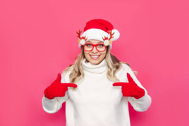 portrait of a beautiful young woman in santa claus hat and gloves over pink background - Foto, immagini