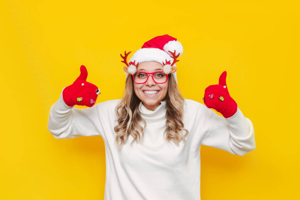 beautiful young woman with christmas hat and gloves showing thumbs up - Foto, immagini