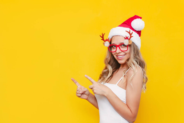 beautiful young woman in santa hat and glasses on yellow background - Фото, зображення