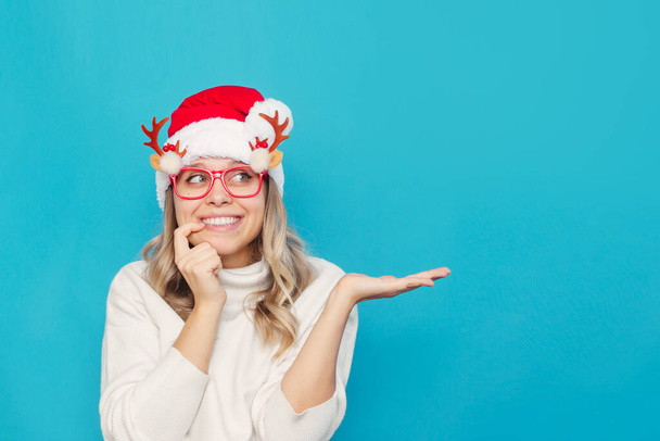 young woman in santa hat and glasses on blue background - Fotoğraf, Görsel