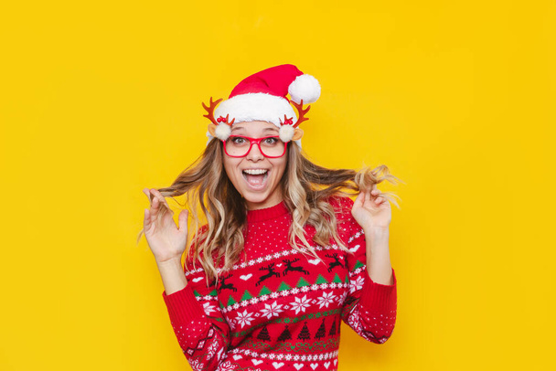 beautiful young woman wearing christmas hat and glasses isolated on yellow background - Fotó, kép