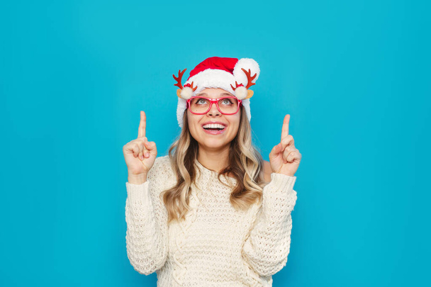 young beautiful woman wearing santa hat and glasses over blue background  - Фото, изображение