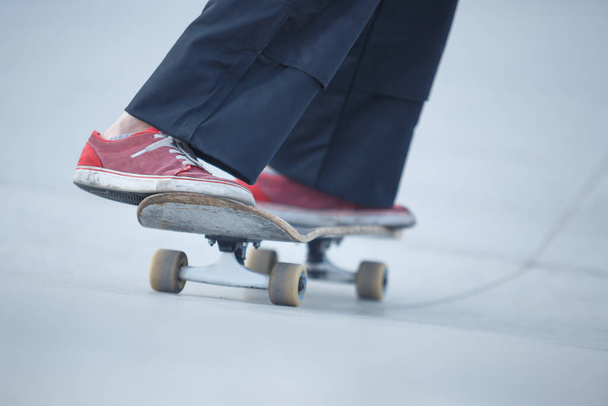 Skater girl rolling on concrete ramp in outdoor skate park. Female skateboarder athlete wearing red shoes - Foto, afbeelding