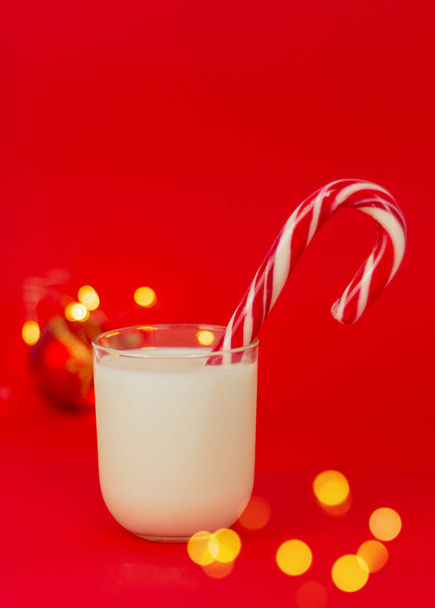 verre de lait avec bonbons de Noël gros plan sur un fond rouge avec des lumières festives. concept de boissons et friandises de Noël pour le Père Noël - Photo, image