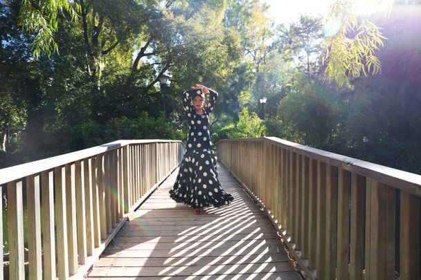hermosa bailarina española morena flamenca con un traje de flamenca típico con lunares blancos bailando en una pasarela de madera en la calle. Patrimonio cultural flamenco de la humanidad. - Foto, imagen