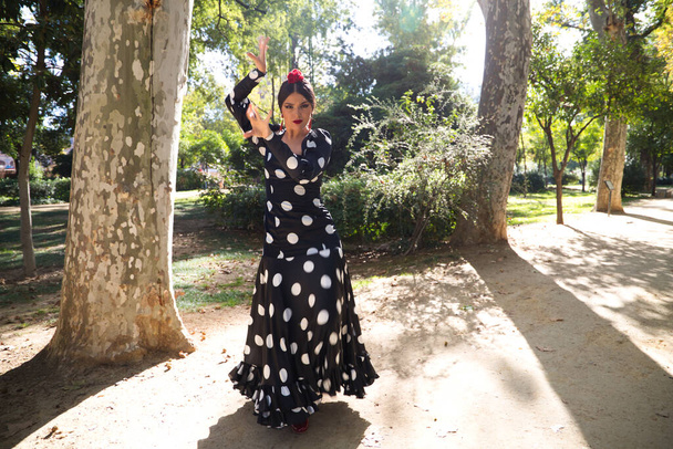 Hiszpańska, piękna, brunetka tancerka flamenco z typową sukienką flamenco w czerni z białymi kropkami polki. Tańczy w parku w Sewilli. Koncepcja Flamenco dziedzictwo kulturowe ludzkości. - Zdjęcie, obraz