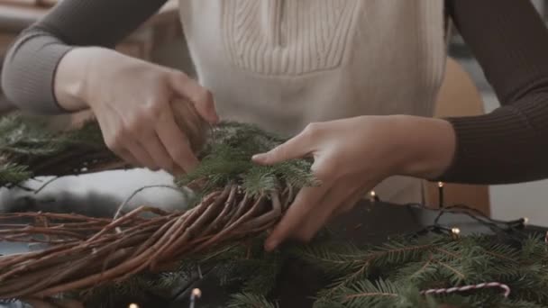 Close-up van de bijgesneden ambachtsman die overdag in haar atelier zit, kerstkrans maakt, met een schaar touw knipt - Video