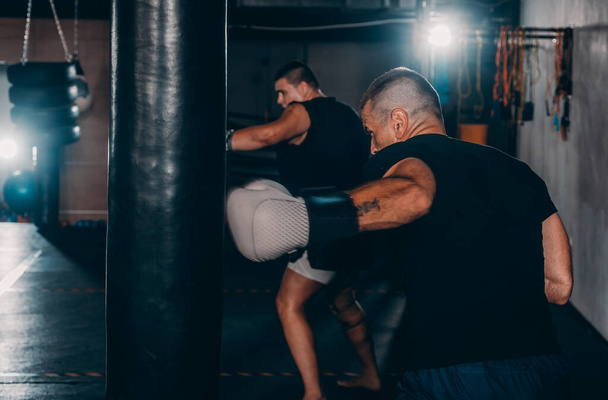 Strong kickboxer man punching black sand bag on gym background - Foto, Bild