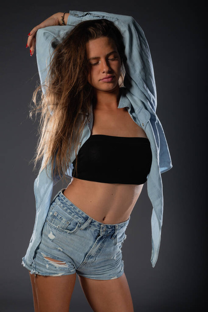 Beautiful young female model in short denim jeans on dark background. - Foto, immagini