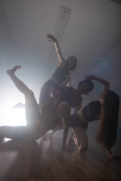 煙と照明で暗いスタジオでファンキーなヒップホップの動きを楽しんでいる多人種のダンサーのグループ。舞台上で活躍する若手ヒップホップダンサーのグループ。幸せな踊りの女性. - 写真・画像