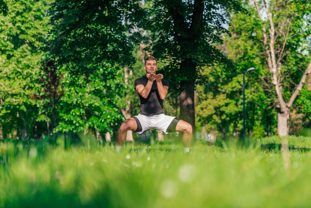 A young man practices yoga with the variations of the goddess pose outdoor in the park - Photo, Image