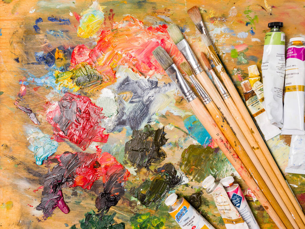 Krasnoyarsk. Russia - August 13, 2021: Artist's palette. Oil art paints extruded onto a wooden palette. Tubes and brushes lie on a colorful board - 写真・画像