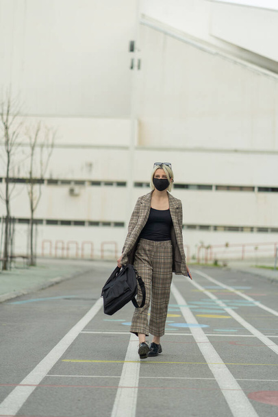 Businesswoman is walking otwards the company while wearing her face mask - 写真・画像