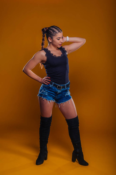 Full-length picture of a pretty urban model posing with her arm at the hip isolated on an orange background - Photo, image