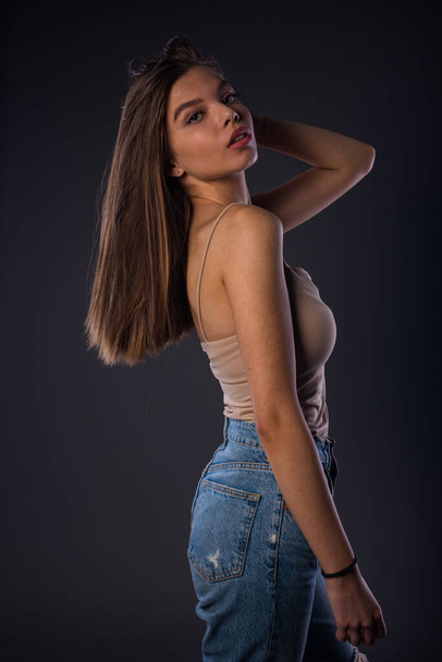 Приваблива молода жіноча модель позує в бежевому баку зверху і джинсових штанях
 - Фото, зображення