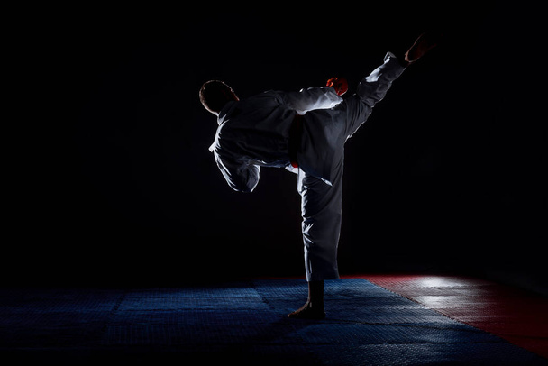 Um jovem homem forte em um quimono branco para sambo, jiu jitsu e outras artes marciais com um treinamento cinto laranja no ginásio - Foto, Imagem
