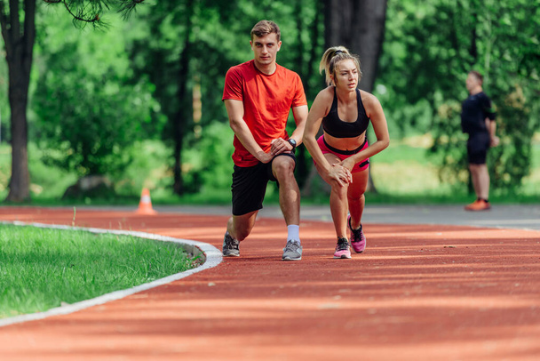Young couple stretching before starting their morning jogging routine on a tartan track at the park. - Photo, Image