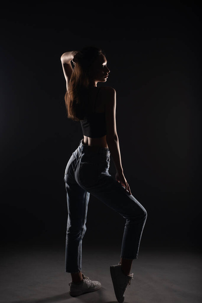 Silhouette of casual dressed and beautiful young girl is posing from the back in studio - Foto, Imagem