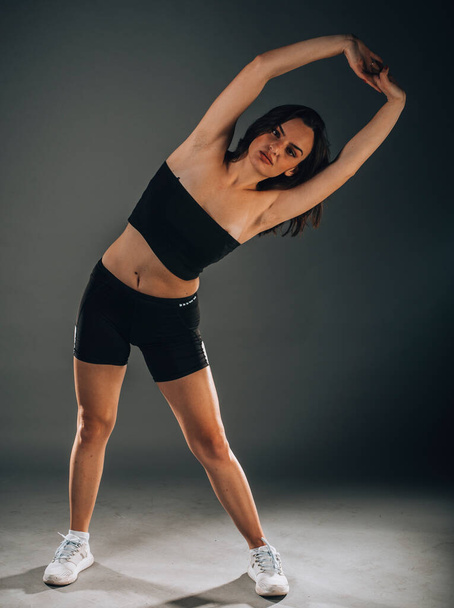 Opgedragen aan fitness. Vooraanzicht van mooie jonge vrouw in sportkleding doen stretching - Foto, afbeelding