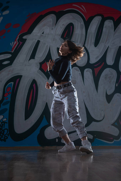 Силуэт молодой женщины-хип-хоп танцовщицы (брейк-дансер), танцующей на фоне студии граффити. Цвета контраста. - Фото, изображение