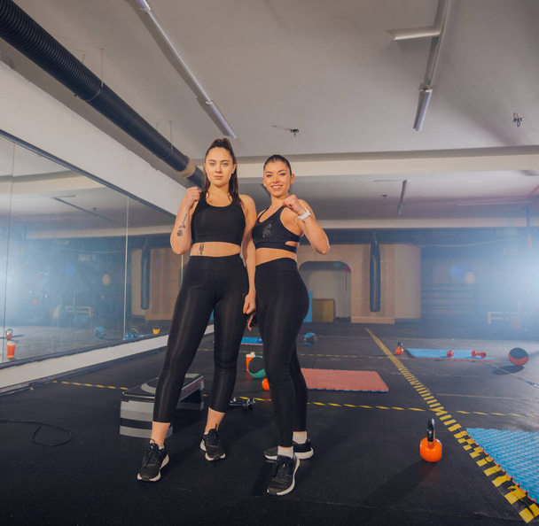 Täyspitkä kuva kaksi vahvaa naista urheiluvaatteet poseeraa kuntosalilla - Valokuva, kuva