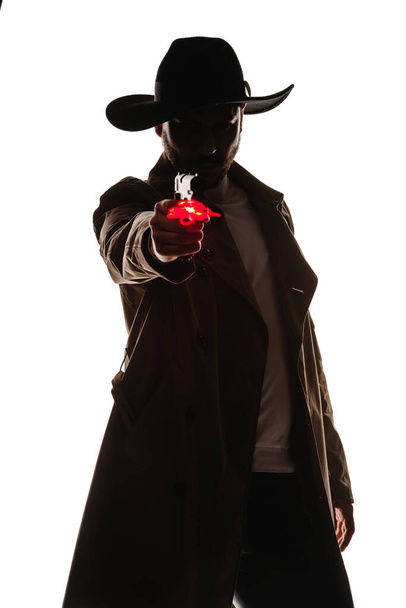 Przystojny młodzieniec ubrany w stylowy strój szeryfa celujący z pistoletu. - Zdjęcie, obraz