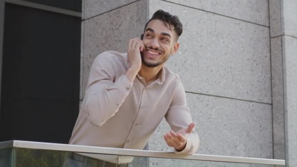 Portré boldog mosolygós spanyol arab férfi spanyol férfi áll erkélyen terasz otthon üzleti iroda beszél mobiltelefon válaszol hívást mosolyogva. Guy beszél okostelefon beszélgetés - Felvétel, videó