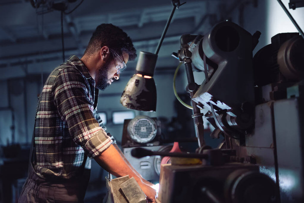 Ritratto di giovane uomo afro-americano concentrato che lavora su cutter indoor in officina metallurgica. - Foto, immagini