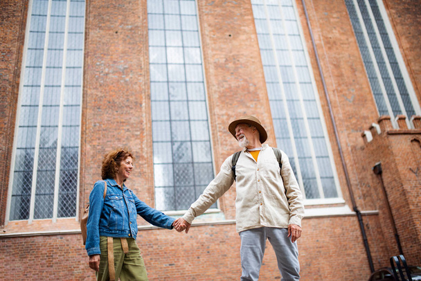 Low angle view of happy senior couple in love holding hands outdoors in town - 写真・画像