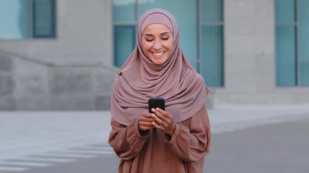 Portrait of muslim young woman user businesswoman islamic girl student in pink hijab on street holding mobile phone using smartphone for chatting browsing typing message smiling shopping online app - Footage, Video