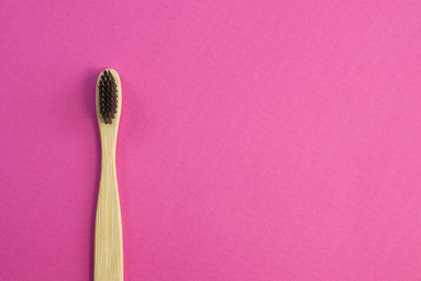 Wooden bamboo toothbrush with black bristles. Natural eco friendly zero waste item on pink background close up - Foto, Bild