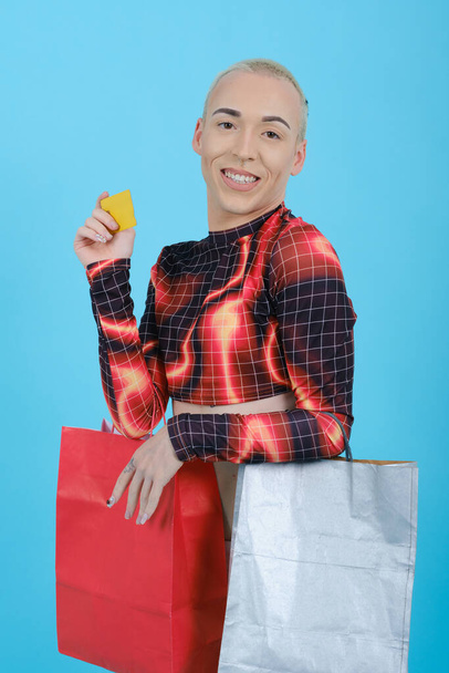 Non-binary person holding a credit card and shopping bags while standing over an isolated background. - Fotografie, Obrázek