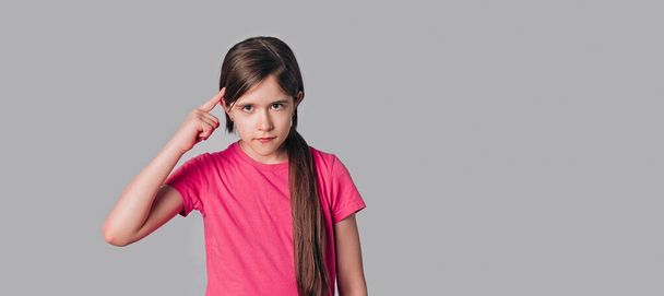 Jong brunette meisje wijzen naar het hoofd met een vinger, geweldig idee of gedachte, goed geheugen, dragen in casual roze t-shirt, staan over grijze achtergrond. Wees slim en denk na. Kopieerruimte - Foto, afbeelding